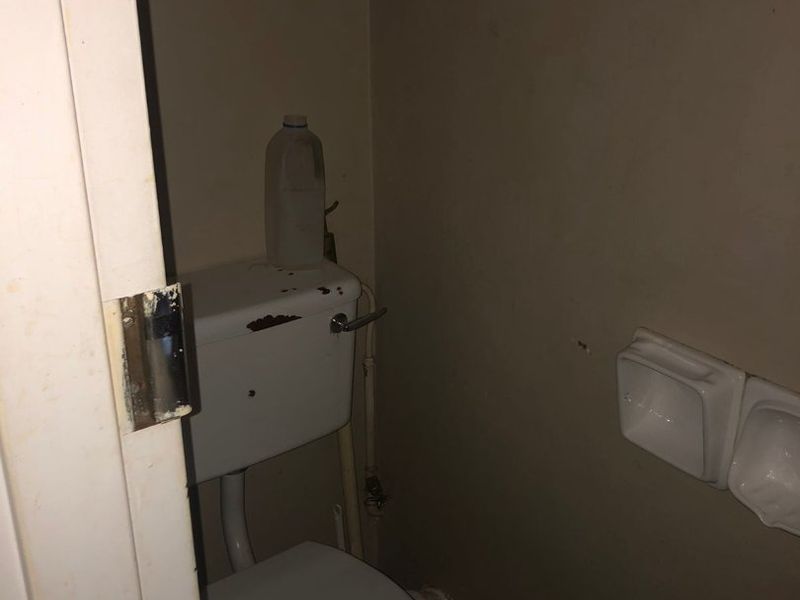 A small, dated bathroom featuring a standard toilet and wall-mounted soap holders, requiring cosmetic updates and maintenance.