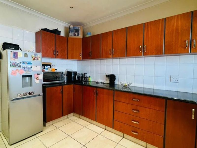 A functional kitchen featuring L-shaped wooden cabinetry, granite countertops, tiled backsplash, and tiled flooring, offering a practical layout for daily meal preparation.