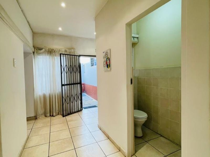 A functional hallway featuring tiled flooring and recessed lighting, providing access to an adjacent bathroom and an exterior doorway with a security gate.