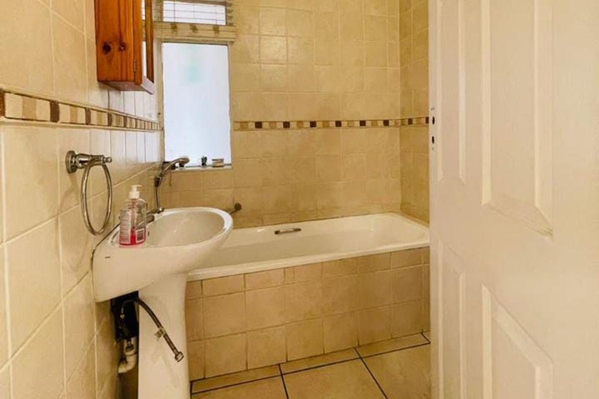 A functional bathroom featuring a pedestal washbasin, a built-in bathtub, and neutral ceramic tiling throughout.