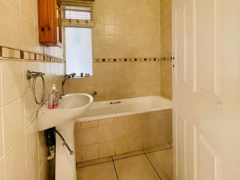 A functional bathroom featuring a pedestal washbasin, a built-in bathtub, and neutral ceramic tiling throughout.