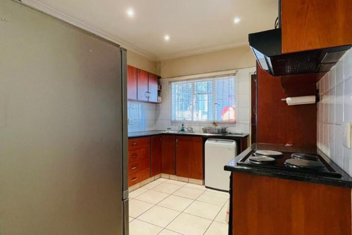 A functional kitchen featuring wooden cabinetry, black granite countertops, an electric hob with extractor fan, and tiled flooring.