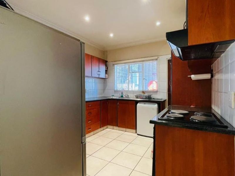 A functional kitchen featuring wooden cabinetry, black granite countertops, an electric hob with extractor fan, and tiled flooring.