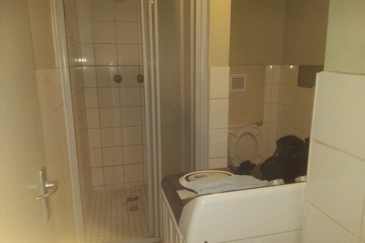A compact bathroom featuring a shower enclosure, toilet, and tiled wall finishes. The space requires maintenance and cosmetic updates.