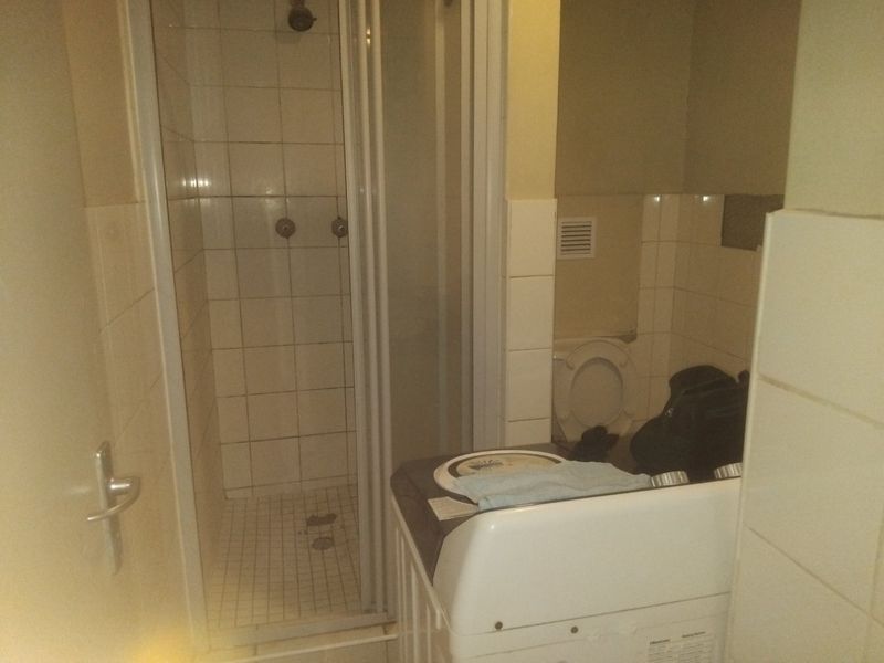 A compact bathroom featuring a shower enclosure, toilet, and tiled wall finishes. The space requires maintenance and cosmetic updates.