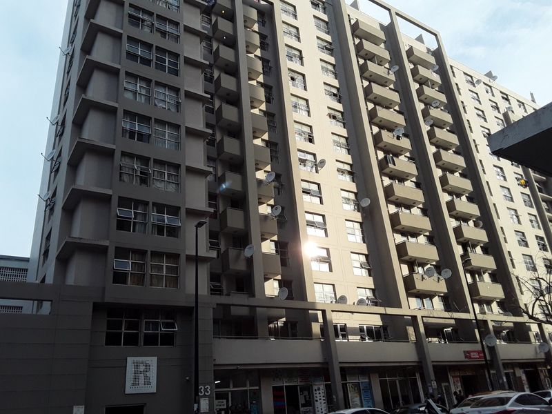 Exterior view of a multi-story apartment building featuring concrete facade, multiple balconies, and ground-level commercial retail spaces.