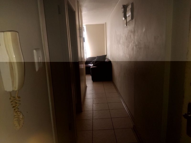 A narrow hallway featuring tiled flooring and an intercom system, showing signs of wall surface wear and requiring cosmetic attention.