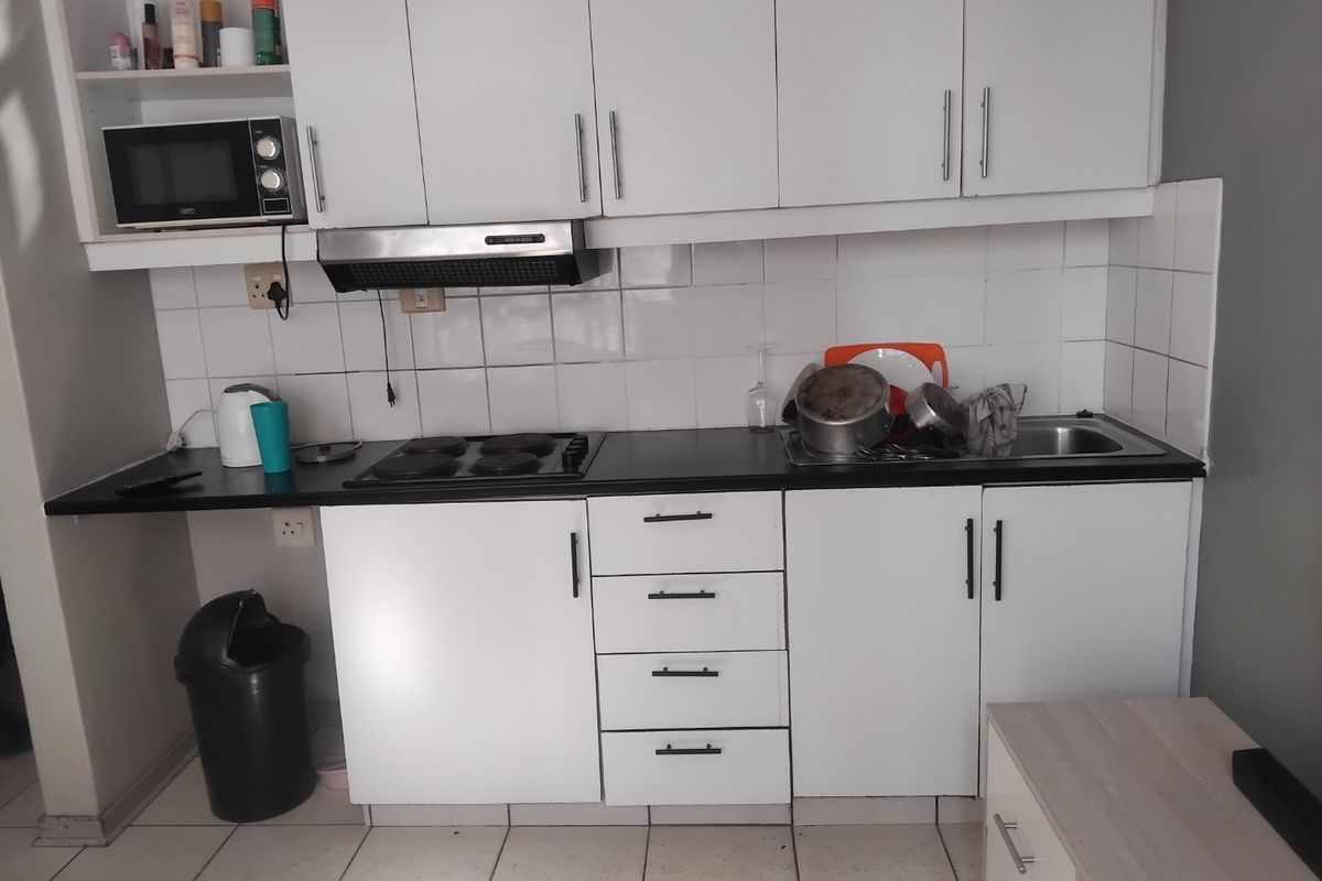 A compact kitchen featuring white cabinetry, a black laminate countertop, an electric hob, and a tiled backsplash.