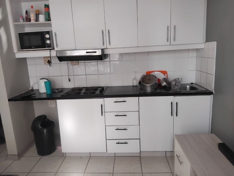 A compact kitchen featuring white cabinetry, a black laminate countertop, an electric hob, and a tiled backsplash.