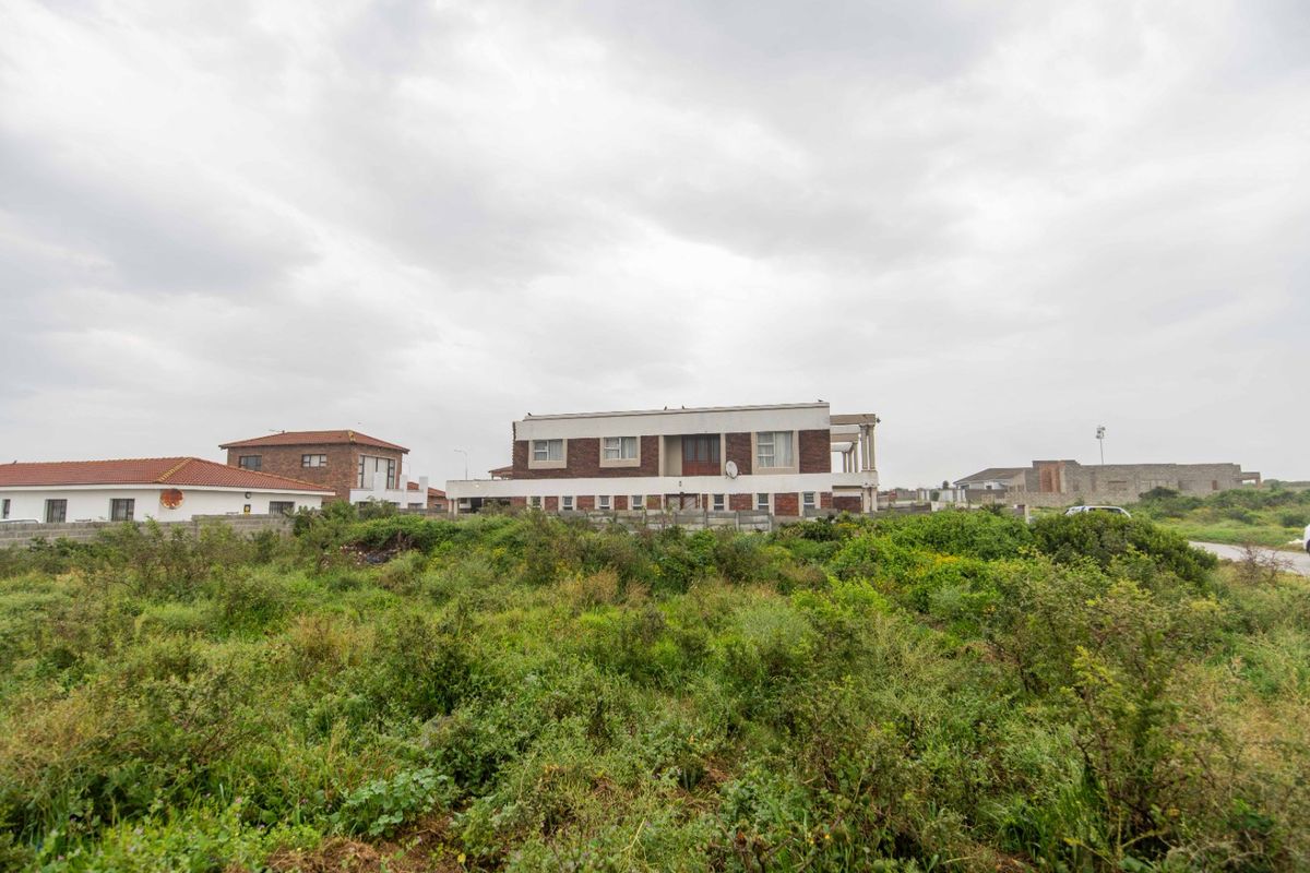 A view of a residential property from an adjacent vacant plot, showing the rear elevation and surrounding boundary walls.
