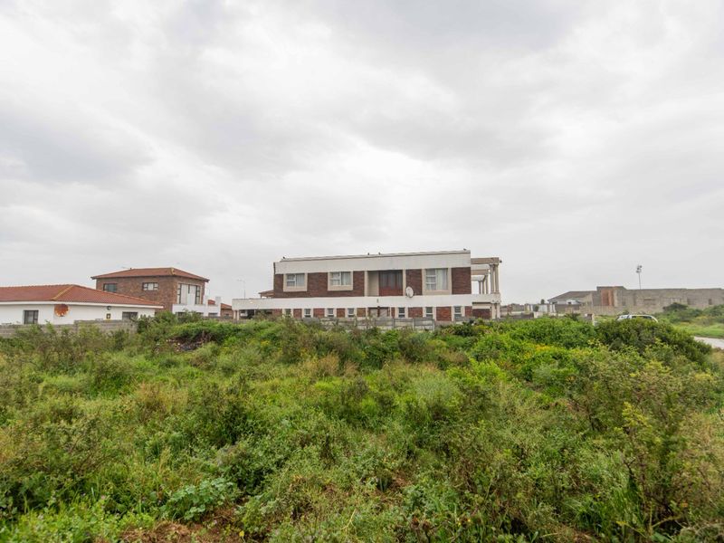A view of a residential property from an adjacent vacant plot, showing the rear elevation and surrounding boundary walls.