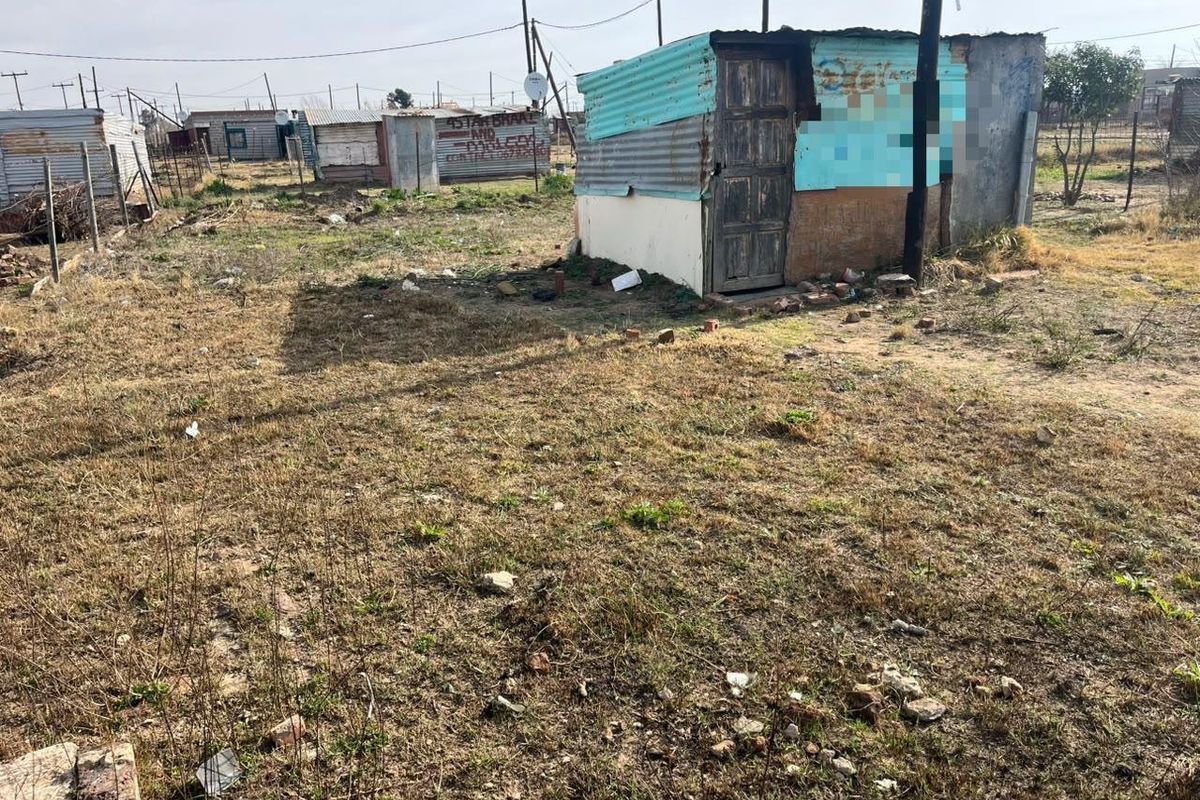 A vacant residential plot featuring a small, dilapidated corrugated iron structure and an utility pole on an unimproved, dry grass lot.