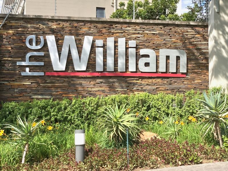 The entrance signage and stone-clad boundary wall of The William apartment complex, featuring well-maintained landscaping and security fencing.