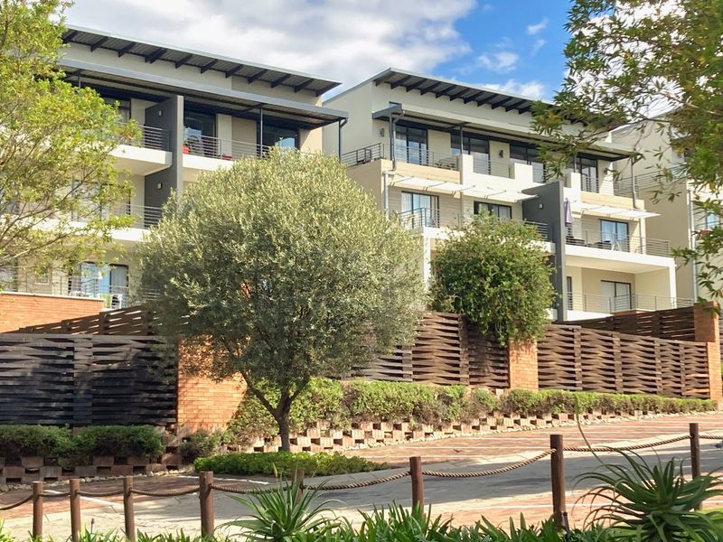 A modern multi-story apartment complex featuring private balconies, decorative timber screening, and well-maintained landscaped grounds with a paved driveway.