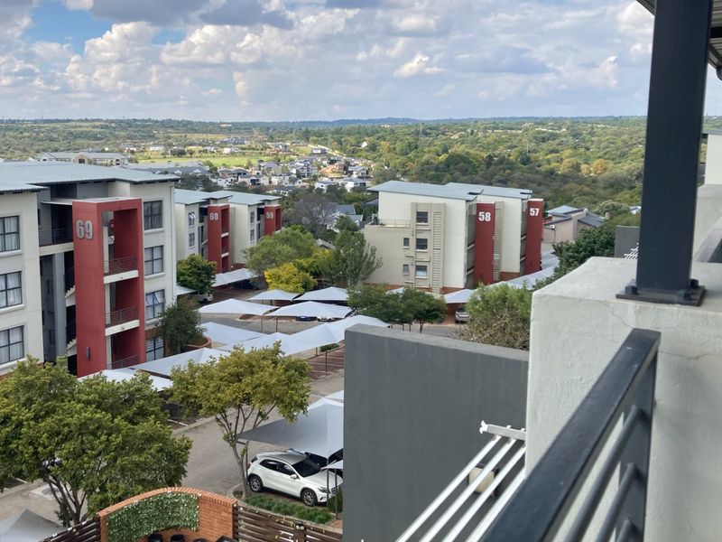 Elevated view overlooking the apartment complex grounds, featuring modern building facades, landscaped areas, and covered parking bays.