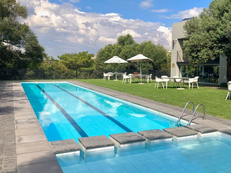 A well-maintained lap swimming pool set within a landscaped garden area, featuring paved surrounds and adjacent lawn space.