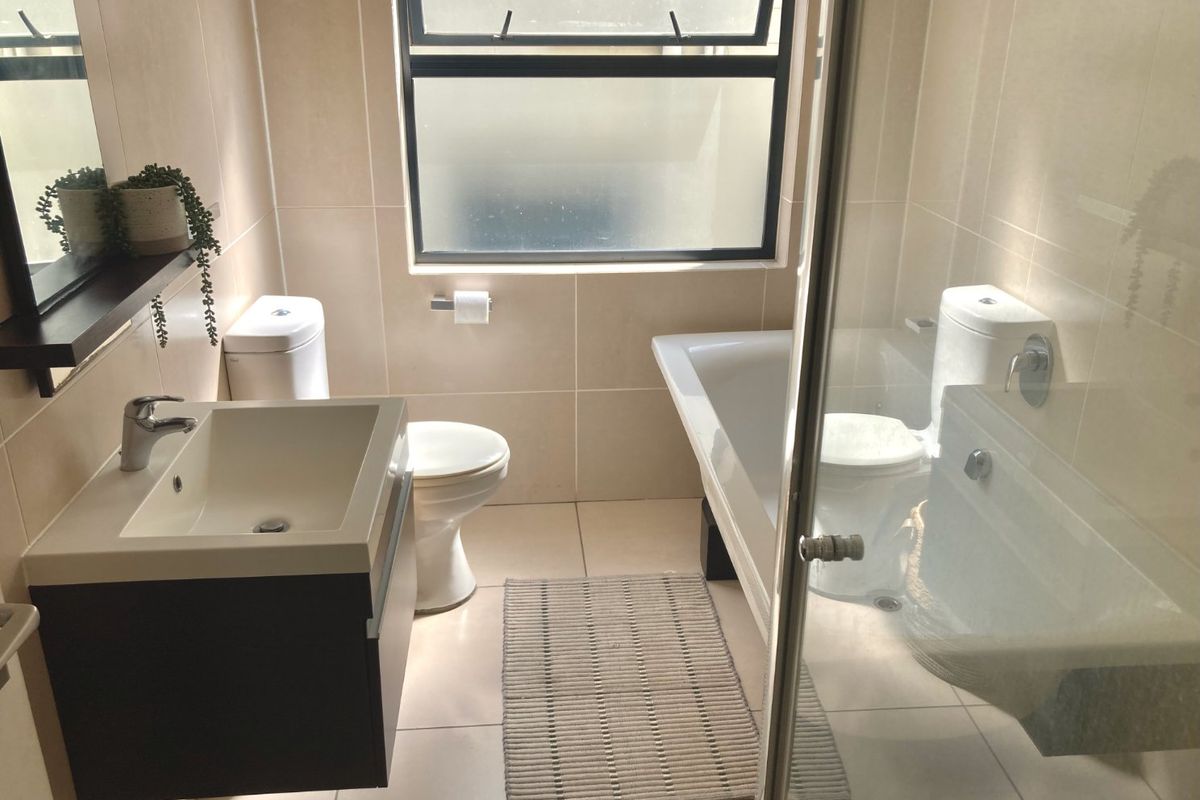 Modern bathroom featuring a wall-mounted vanity, basin, toilet, bathtub, and a glass shower screen with neutral floor-to-ceiling tiling.