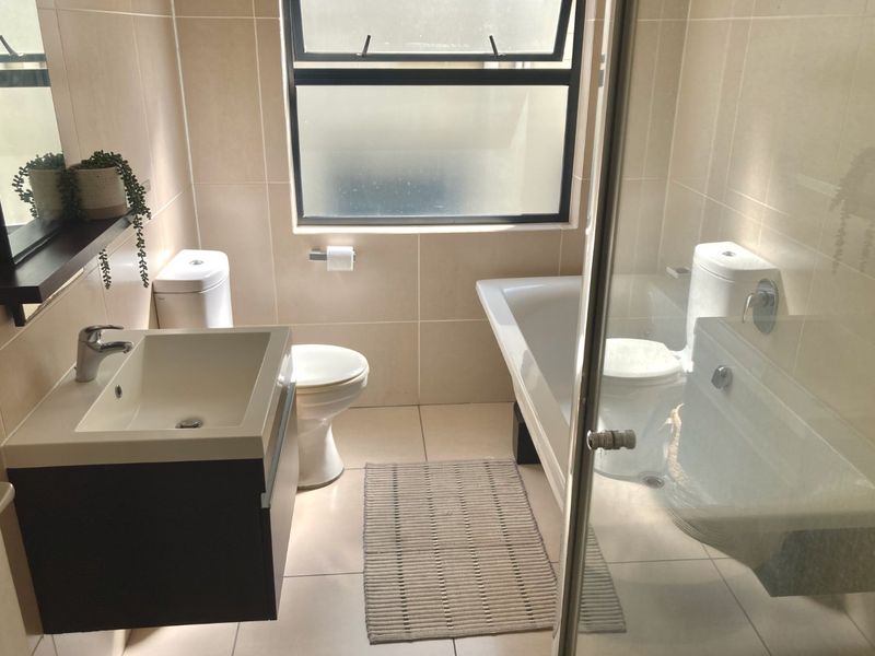 Modern bathroom featuring a wall-mounted vanity, basin, toilet, bathtub, and a glass shower screen with neutral floor-to-ceiling tiling.