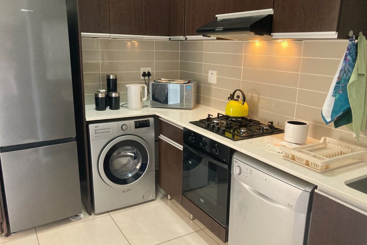 A compact, modern kitchen featuring dark wood cabinetry, stone countertops, a gas hob, built-in oven, and integrated extractor fan with tiled backsplash.
