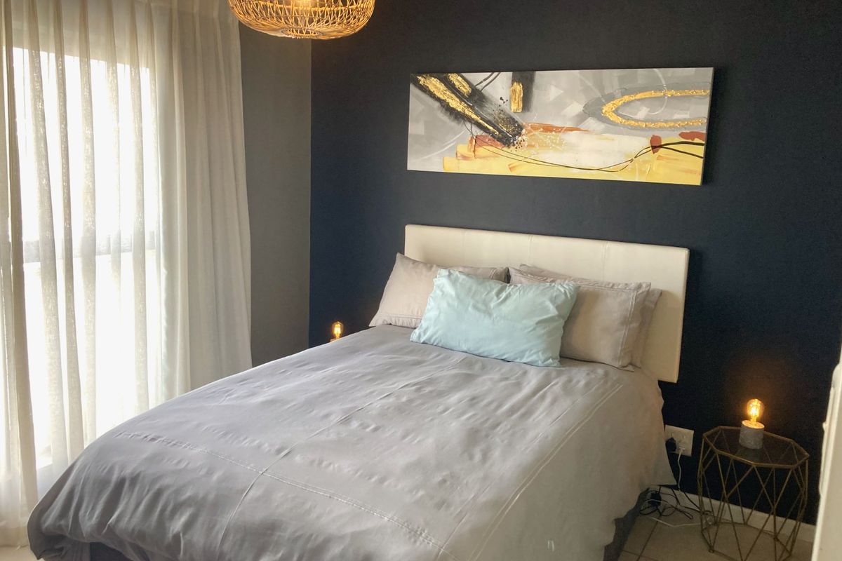 A well-maintained bedroom featuring a dark accent wall, tiled flooring, and large windows allowing for natural light.