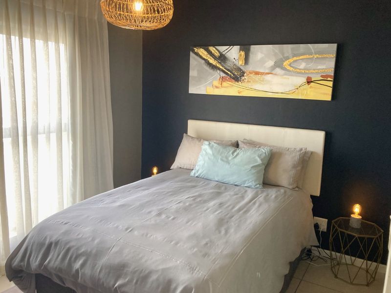 A well-maintained bedroom featuring a dark accent wall, tiled flooring, and large windows allowing for natural light.