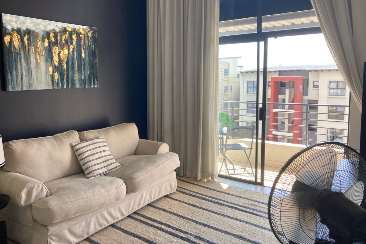 A living room featuring a dark accent wall and a sliding glass door that opens onto a private balcony with neighborhood views.