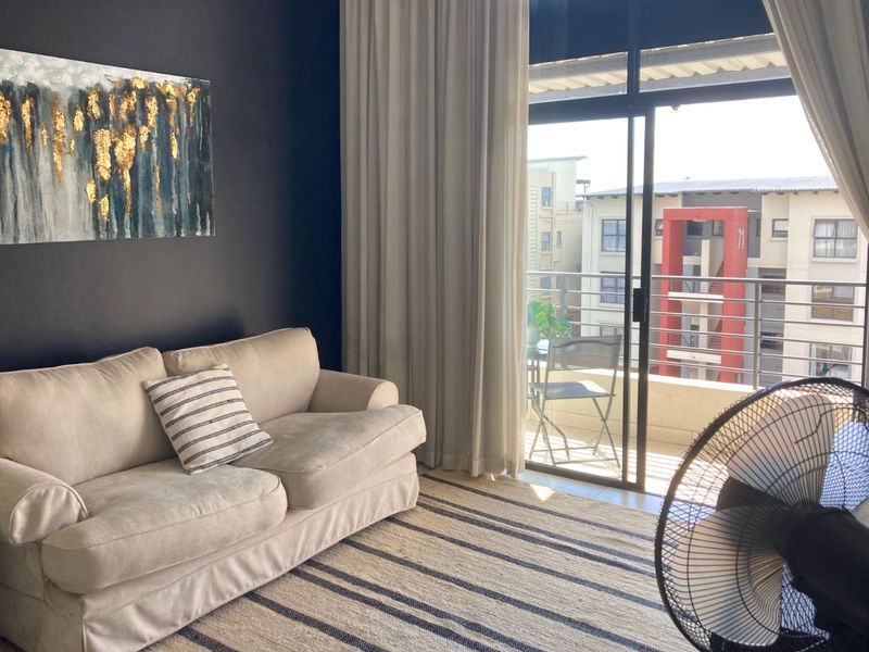 A living room featuring a dark accent wall and a sliding glass door that opens onto a private balcony with neighborhood views.