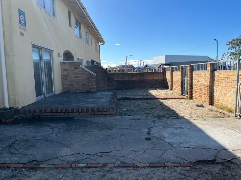 Rear exterior view featuring a paved patio area, brick boundary walls, and a concrete driveway with visible surface cracking.