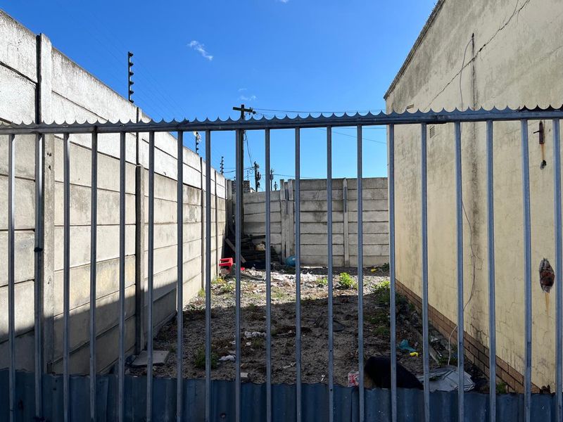 A narrow, enclosed rear yard area featuring precast concrete boundary walls, steel palisade fencing, and electric security wiring.