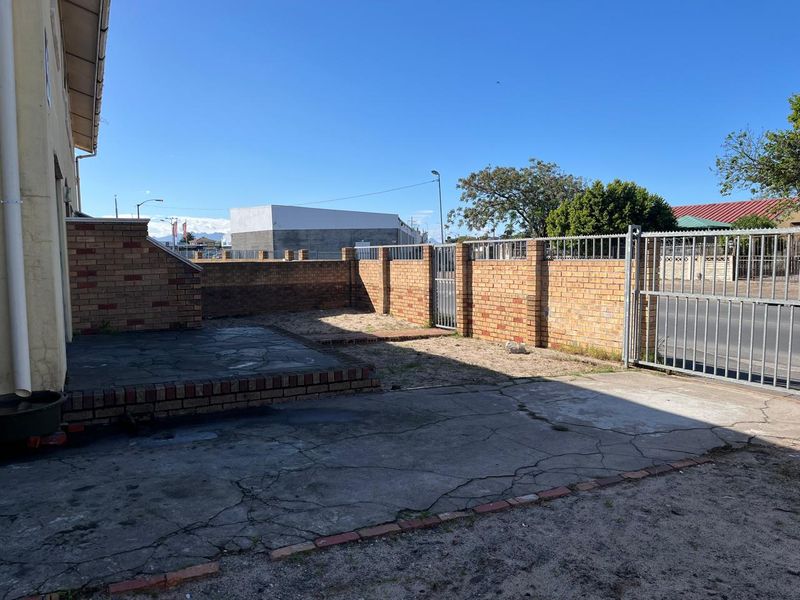 Rear exterior area featuring a paved patio, face brick boundary walls, and a metal security gate with access to the driveway.