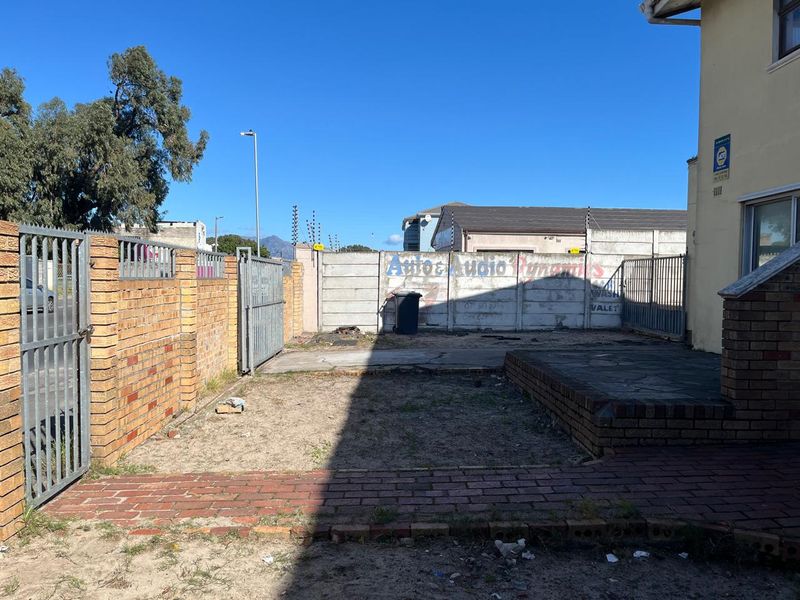 Rear exterior area featuring a brick boundary wall, metal security gate, paved walkway, and a raised brick patio.
