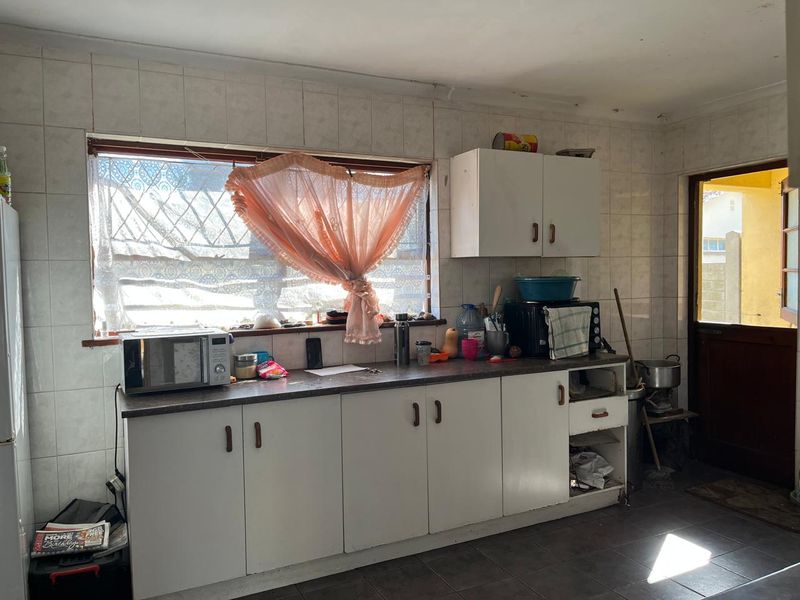 A functional kitchen featuring tiled walls and floors, laminate countertops, and built-in cabinetry, requiring some maintenance and cosmetic updates.