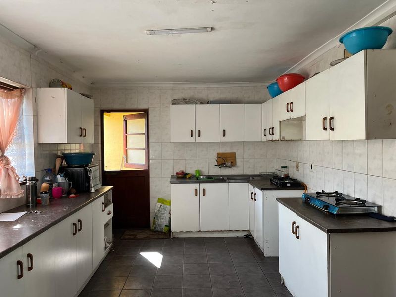 A functional kitchen featuring white built-in cabinetry, laminate countertops, a gas hob, and tiled finishes, offering potential for a modern renovation.