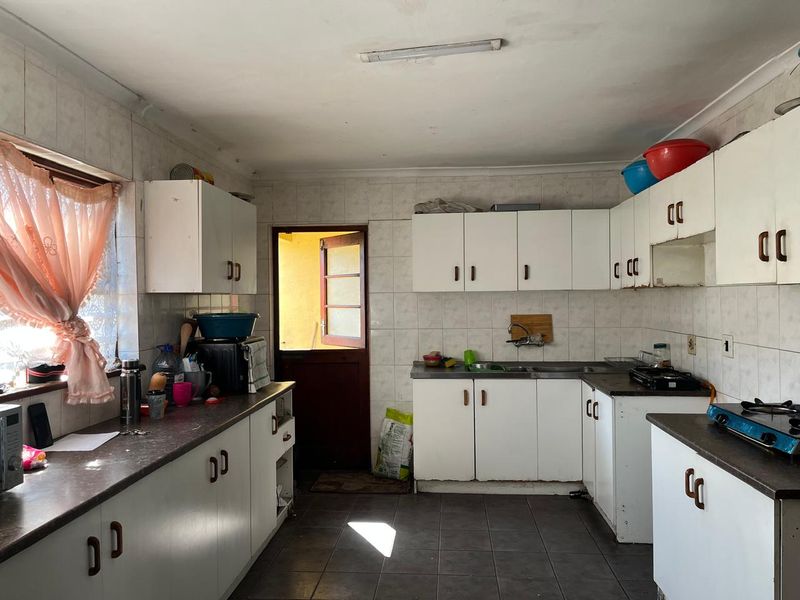 A functional kitchen featuring white built-in cabinetry, dark laminate countertops, tiled backsplash, and tiled flooring, offering potential for modernization.