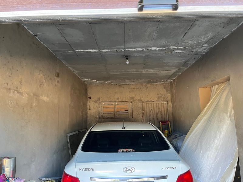 A functional garage space featuring concrete ceiling panels, a security gate, and a louvered window, currently requiring cosmetic updates and wall finishing.