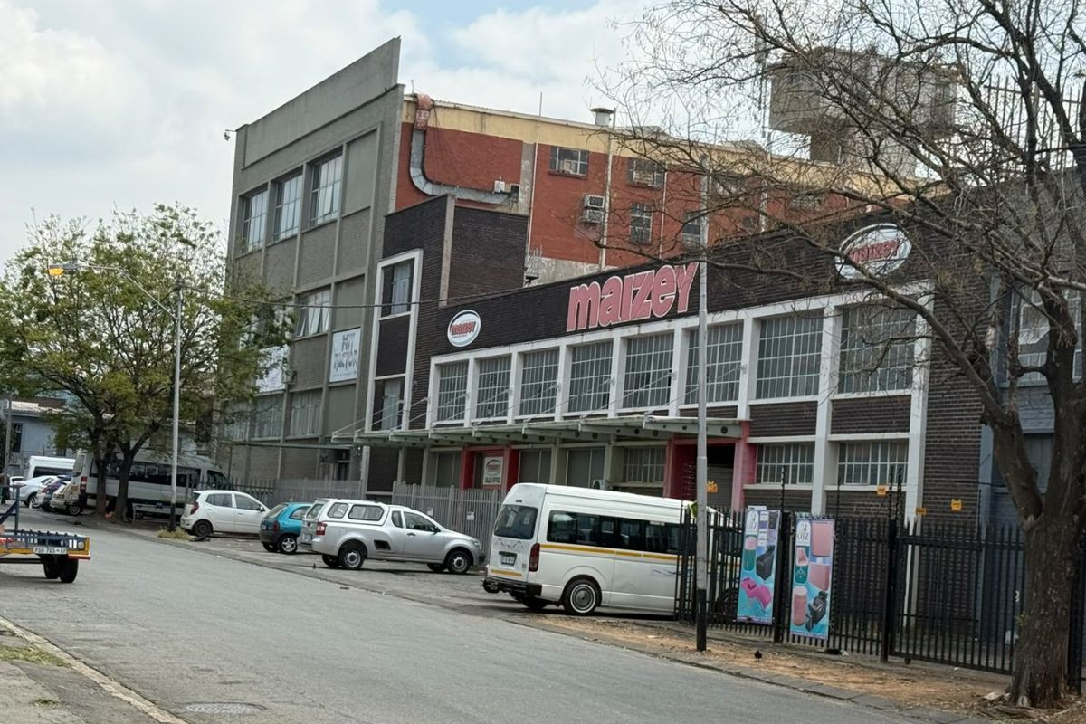Street-level view of a multi-story industrial property featuring brick facade, metal window frames, and secure perimeter fencing.
