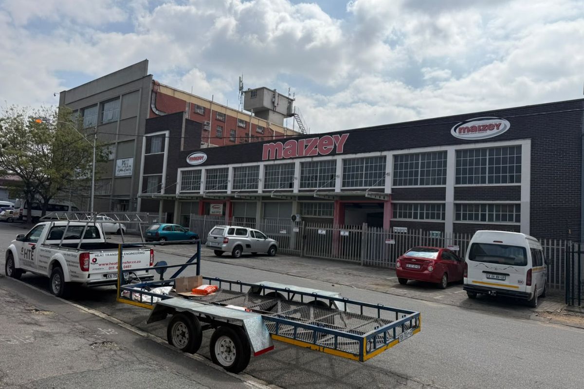 Front elevation of an industrial warehouse facility featuring brick construction, large multi-pane windows, and secure perimeter fencing with roller shutter access.