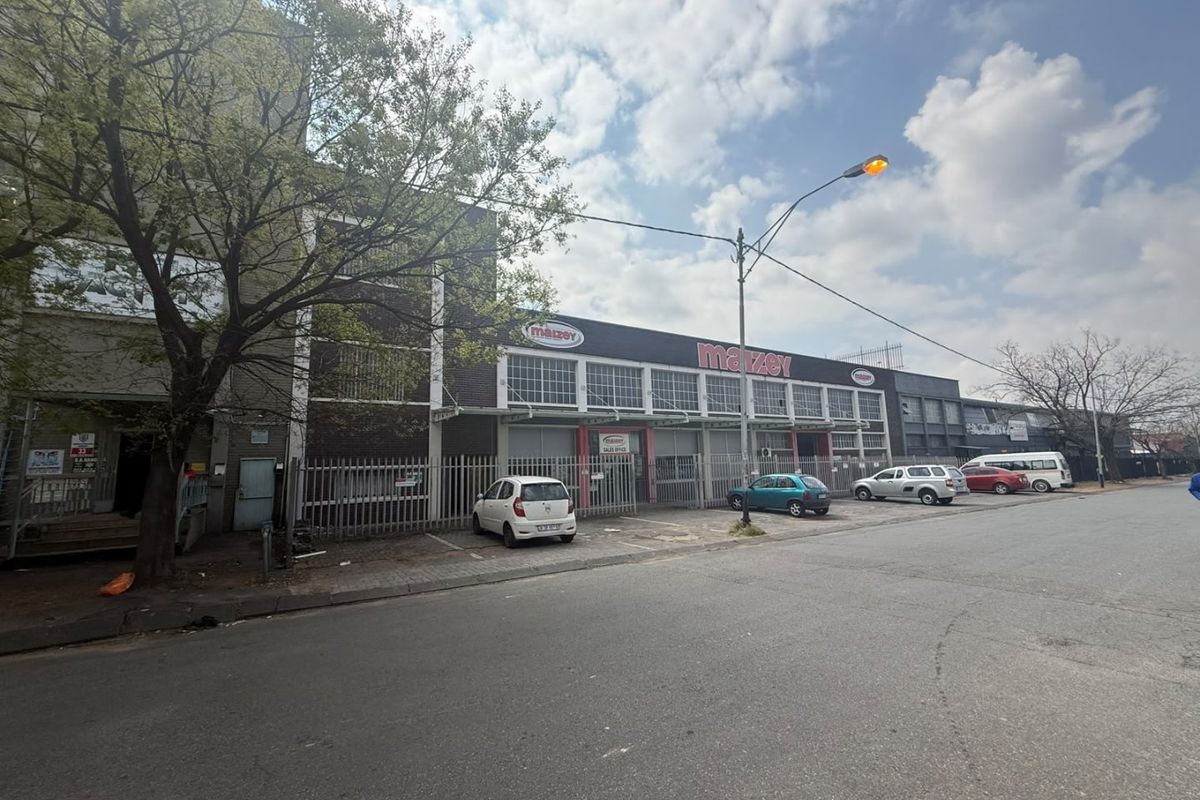 Front exterior view of an industrial property featuring a brick facade, security fencing, and dedicated street-level parking.