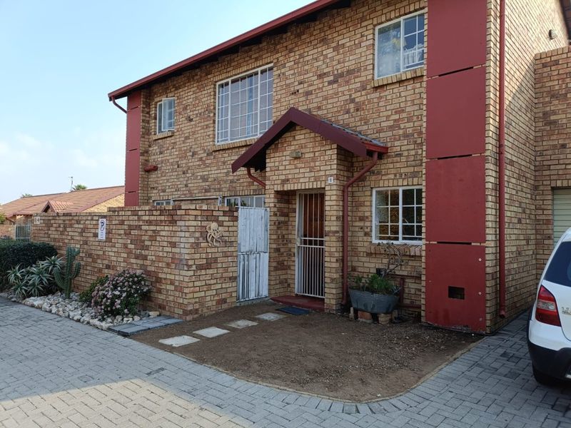 Front elevation of a face brick apartment unit featuring a covered entrance, security gate, and paved driveway access.
