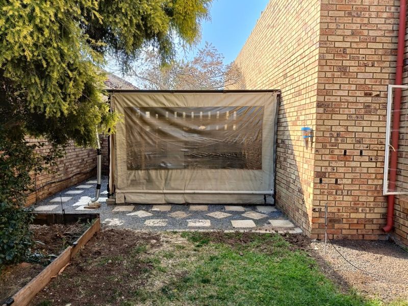 Rear exterior view featuring a brick facade, a paved patio area with a canvas enclosure, and a small garden space.