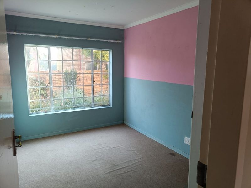 An empty bedroom featuring carpeted flooring, a large window with security bars, and dual-tone painted walls.