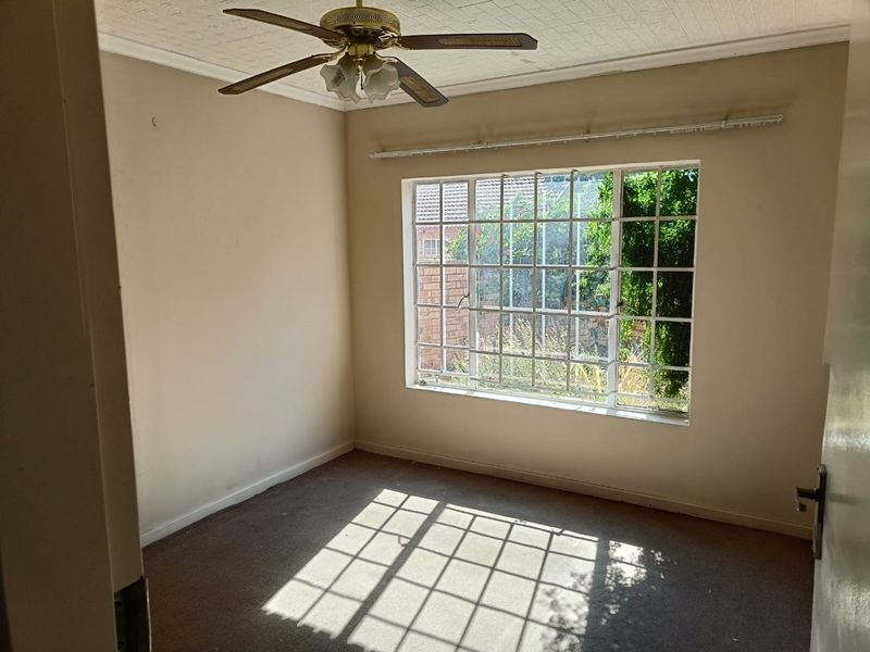 An empty bedroom featuring a ceiling fan, carpeted flooring, and a large grid-pattern window allowing natural light.