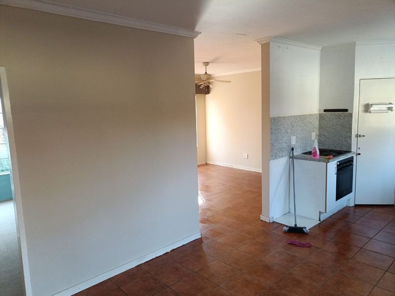 Open plan living and kitchen area featuring tiled flooring, built-in oven, and cooktop, offering a blank canvas for renovation and interior design.