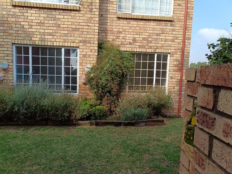 A rear view of the apartment building featuring a face brick facade, grid-pattern windows, and a small private garden area with a brick boundary wall.