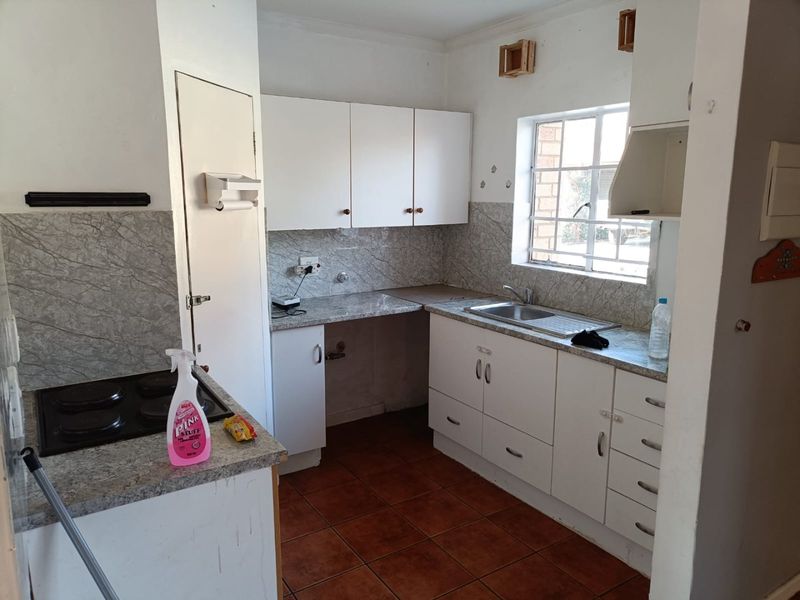 A functional kitchen featuring white cabinetry, laminate countertops, a stainless steel sink, and an electric hob, ready for modernization and cosmetic updates.
