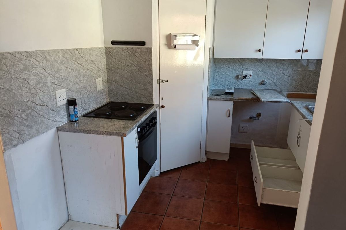 A functional kitchen featuring built-in oven, electric hob, tiled backsplash, and ample cabinetry, currently requiring some maintenance and cosmetic updates.