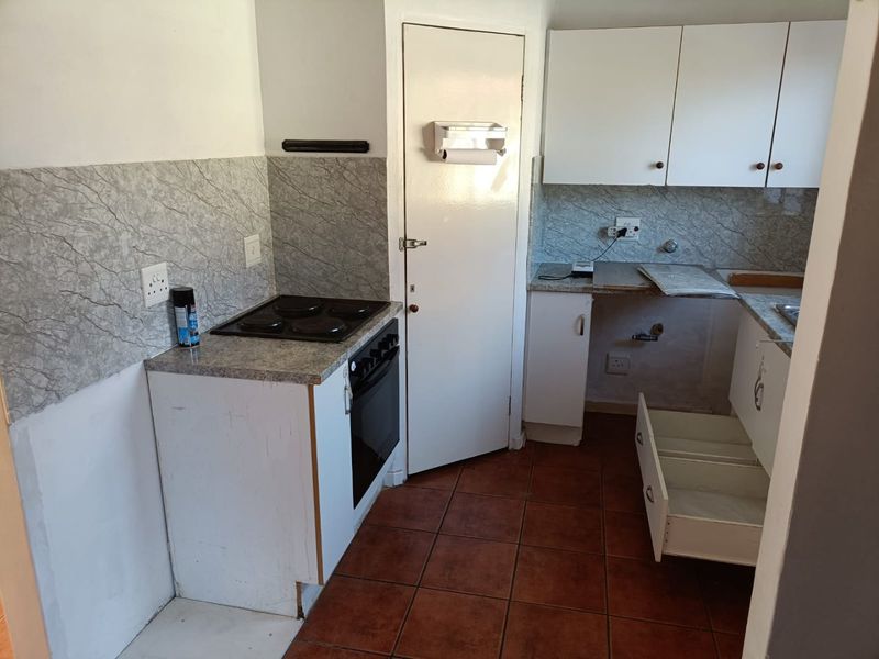 A functional kitchen featuring built-in oven, electric hob, tiled backsplash, and ample cabinetry, currently requiring some maintenance and cosmetic updates.