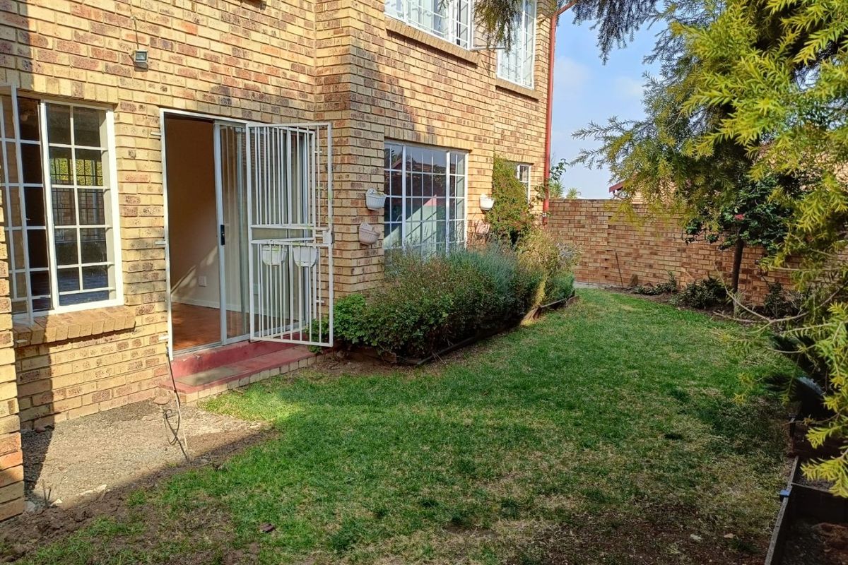 Rear view of a face brick apartment building featuring a small private garden, lawn, and a sliding door with a security gate.