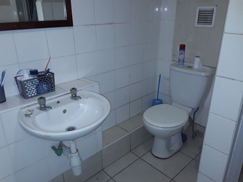 A functional bathroom featuring a pedestal washbasin, standard toilet, and white ceramic wall and floor tiling.