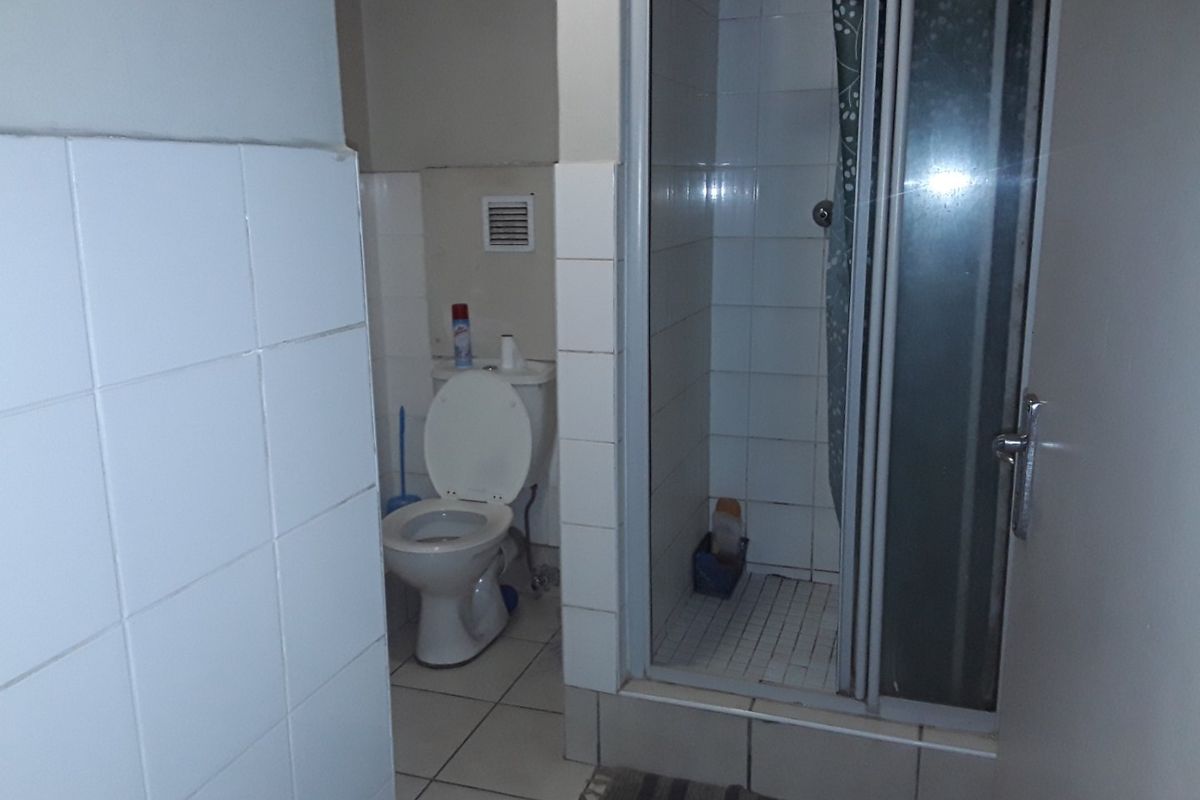 A functional bathroom featuring a shower enclosure, toilet, and tiled finishes throughout, presenting an opportunity for modernization and cosmetic updates.